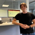 Ein Mitarbeiter von MINDA lehnt an einem Schreibtisch mit 2 Monitoren