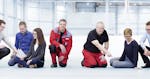 Seven MINDA employees sit or squat on the floor. The clothing styles range from work clothes to suits and thus represent the different areas of the company.