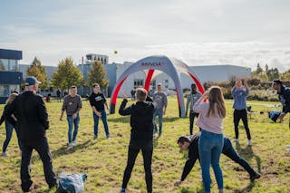 Spielerisches Teambuilding: Azubi und Studenten lernen sich bei Teamevent standortübergreifend besser kennen. Mehrere Mitarbeiter von MINDA stehen vor dem MINDA-Firmengebäude bei Sonnenschein an der frischen Luft