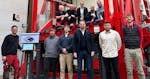 The photo shows a group picture with a team in front of a compact crane.